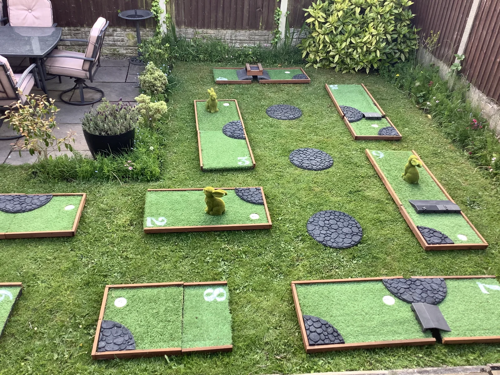 Mini golf holes on a garden lawn beside a patio, planting and timber fencing