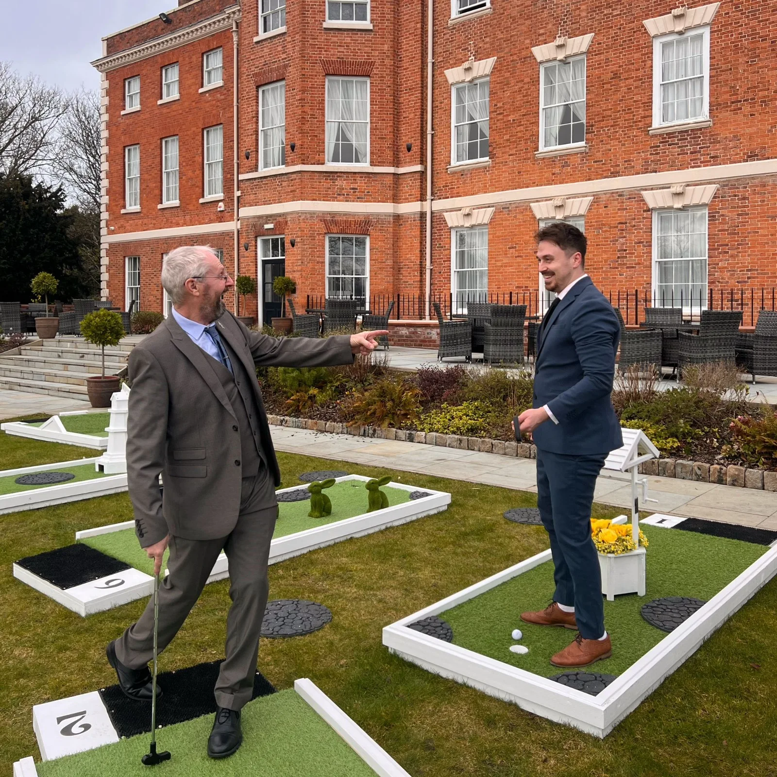 Two guests with putters enjoying the Fairway course outside a red-brick building