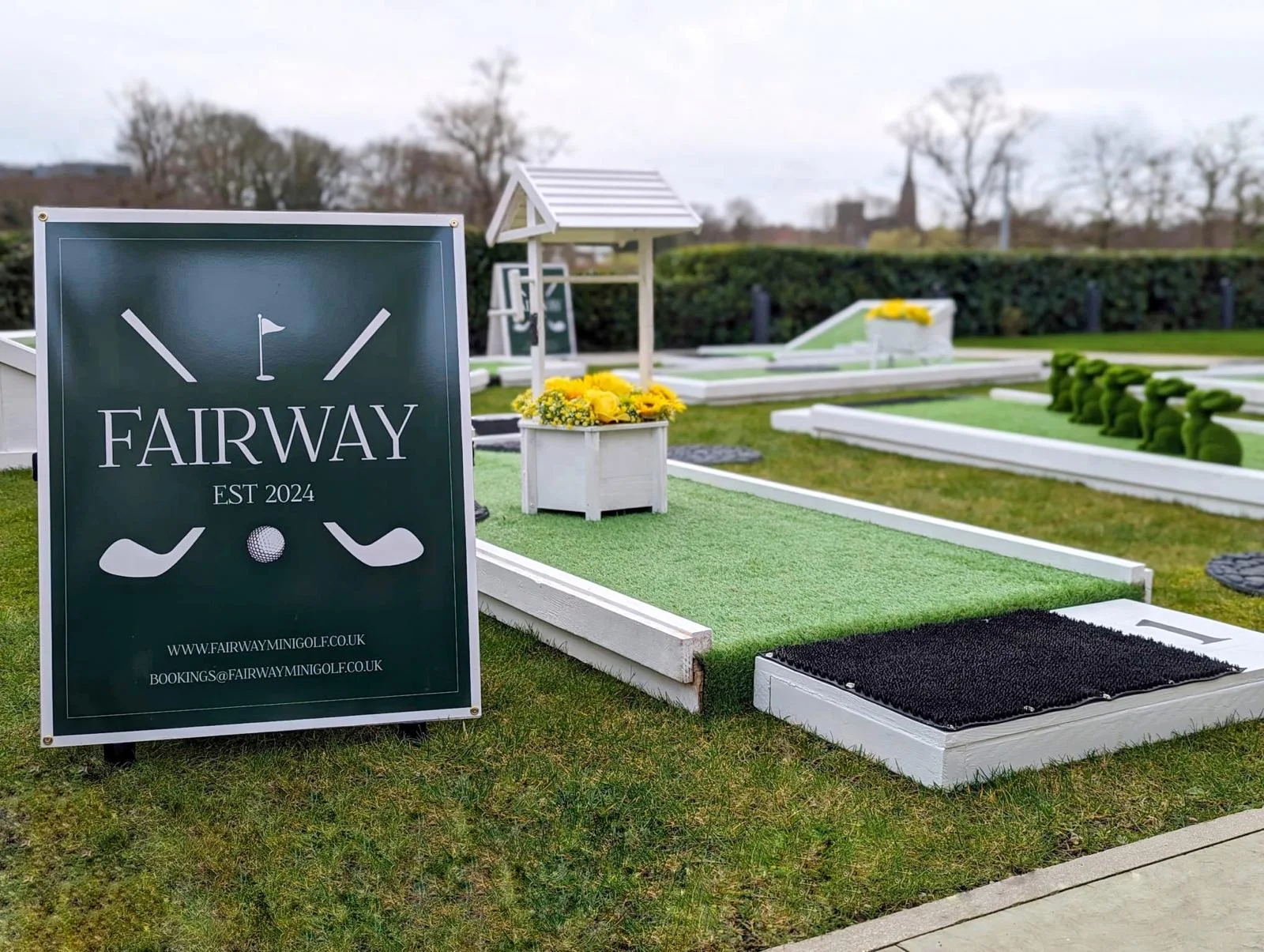 Fairway sign beside a white wishing-well obstacle and green putting surface